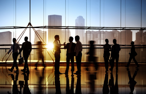 A group of silhouetted office workers congregate on a polished floor of a skyscraper building at sunset.